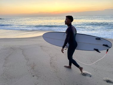 sörfçü dalgaları ile sahilde günbatımı Portekiz'de yürüyüş.