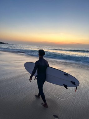 sörfçü dalgaları ile sahilde günbatımı Portekiz'de yürüyüş.