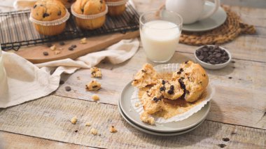 Chocolate chip muffins with milk served on glass cups on white kitchen countertop.