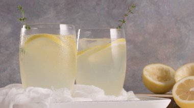 Soğuk limonata veya alkollü kokteyl limon, biberiye ve hafif bir arka plan üzerinde cam bardaklarda buz ile.