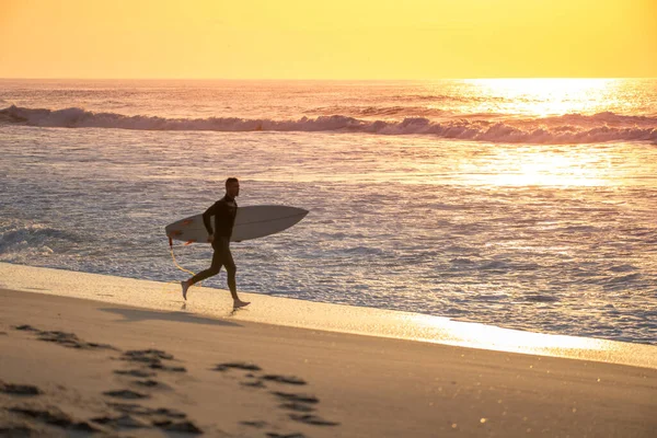 Surfer running on the beach with the waves at sunset in Portugal.