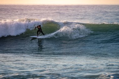 Cesur genç gün batımında dalgalı denizde numaralar yapıyor..