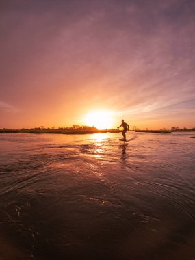 Günbatımında Portekiz 'deki Ria de Aveiro kanallarından birinde sörf tahtasıyla suda süzülüyor..