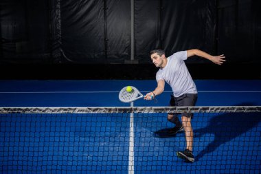 Kapalı alanda padel oynayan genç sporcu Padel oyuncusu raketle topa vuruyor..