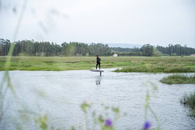 Bulutlu bir günde Portekiz 'deki Ria de Aveiro kanallarından birinde sörf tahtasıyla suyun üzerinde süzülüyor..