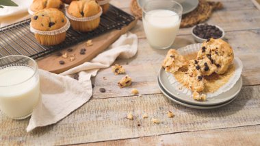 Chocolate chip muffins with milk served on glass cups on white kitchen countertop.