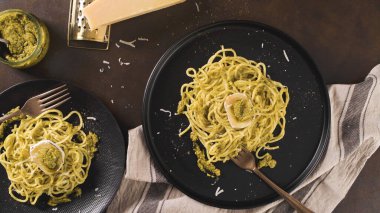 Karanlık mutfak tezgahında fesleğen soslu ve peynirli taze spagetti..