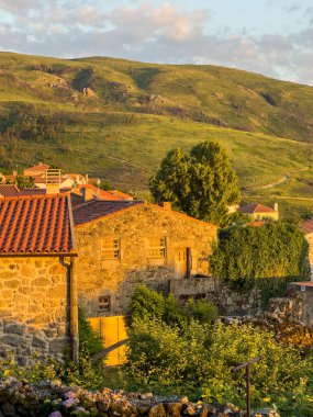 Golden hour over a rustic village with stone houses nestled among green hills. Linhares da Beira, Portugal. clipart