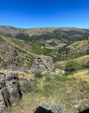 Berrak mavi gökyüzünün altında dolambaçlı tren yolu ve kayalık arazisi olan yemyeşil bir vadi. Guarda, Portekiz.