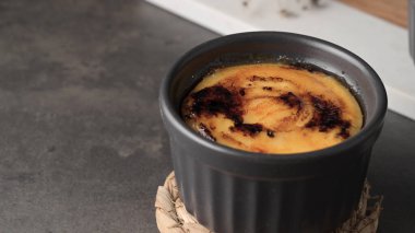 A close-up of a creme brule in a black ramekin on a woven coaster. clipart