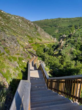 Berrak mavi gökyüzünün altındaki yemyeşil dağların arasından geçen ahşap bir yolda huzurlu bir yolculuk bekliyor. Guarda - Portekiz.