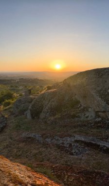 Sıcak gün batımı parlaklığı engebeli araziyi yıkar, huzurlu ve geniş bir manzara sunar. Guarda - Portekiz.