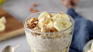 Muz dilimleri ve bademlerle kaplı iki kase yulaf. Bir kaşık, kesme tahtası, bıçak ve yanında mavi bir peçete..