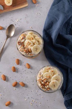 Muz dilimleri ve bademlerle kaplı iki kase yulaf. Bir kaşık, kesme tahtası, bıçak ve yanında mavi bir peçete..