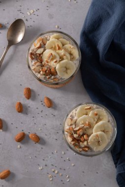 Muz dilimleri ve bademlerle kaplı iki kase yulaf. Bir kaşık, kesme tahtası, bıçak ve yanında mavi bir peçete..
