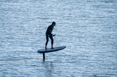 Sörfçü, sakin bir deniz ortamındaki gelişmiş su sporları teknolojisini gösteren elektrikli su folyosunun üzerinde süzülüyor.