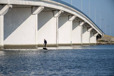 Hidrofolyo sörfçüsü devasa beton köprünün altında süzülerek, sakin sularda kentsel altyapı ile modern su sporları teknolojisini birleştiriyor..