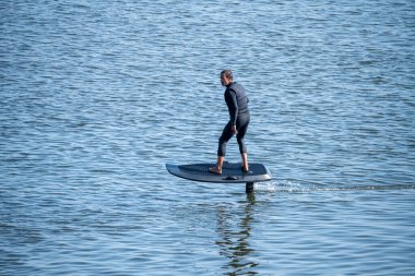 Man on an eFoil board gliding over calm blue water, showcasing balance and modern water sport technology clipart