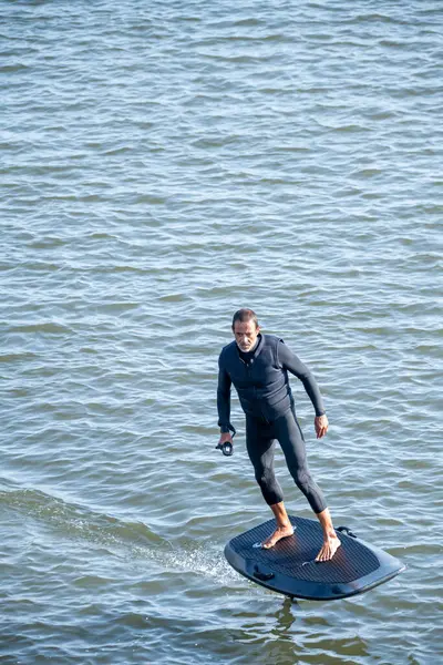 Stock image Hydrofoiling on a calm blue sea, a person showcases balance and skill, gliding effortlessly on the water surface under a sunny sky.