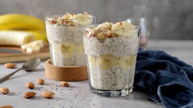 Muz dilimleri ve bademlerle kaplı iki kase yulaf. Bir kaşık, kesme tahtası, bıçak ve yanında mavi bir peçete..