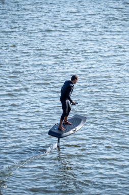 Sörf tahtasındaki siluetli adam su yüzeyinde süzülüyor..