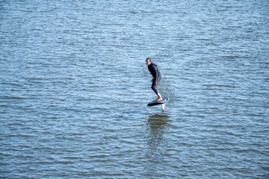 Sörf tahtasındaki siluetli adam su yüzeyinde süzülüyor..