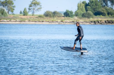Sörf tahtasındaki siluetli adam su yüzeyinde süzülüyor..
