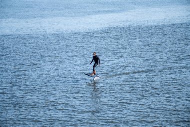 Silhouetted man on a hydrofoil surfboard gliding above water surface. clipart