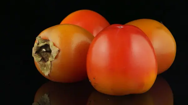 stock image Red ripe persimmons rotating over black background.