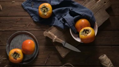 Kırsal bir ahşap masa üzerinde olgun hurmalar, mavi bir bez ve bir kesim tahtasıyla.