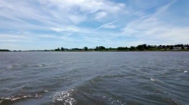 Geniş göl manzarası, ince bulutların altında dalgalanan sular, uzak ağaçlarla kaplı kıyılar ve parlak bir günde rıhtım boyunca dağınık binalar. Ovar, Aveiro - Portekiz.