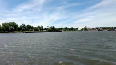 Geniş göl manzarası, ince bulutların altında dalgalanan sular, uzak ağaçlarla kaplı kıyılar ve parlak bir günde rıhtım boyunca dağınık binalar. Ovar, Aveiro - Portekiz.