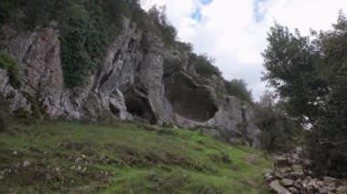 Buracas do Casmilo at Condeixa - Portekiz. Engebeli bir yamaçta yuva yapmış antik kireçtaşı mağaraları, bulutlu bir günde yeşil bitki örtüsü ve yosun kaplı kaya oluşumları arasında birden fazla doğal mağara açıkları barındırır..