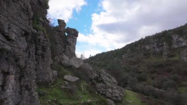 Buracas do Casmilo at Condeixa - Portekiz. Engebeli bir yamaçta yuva yapmış antik kireçtaşı mağaraları, bulutlu bir günde yeşil bitki örtüsü ve yosun kaplı kaya oluşumları arasında birden fazla doğal mağara açıkları barındırır..