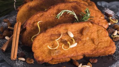 Traditional Christmas Rabanadas with lemon zest, raisins, pine nuts and cinnamon. Spanish Torrijas or french toasts close up on the countertop clipart