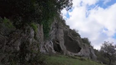 Buracas do Casmilo at Condeixa - Portekiz. Engebeli bir yamaçta yuva yapmış antik kireçtaşı mağaraları, bulutlu bir günde yeşil bitki örtüsü ve yosun kaplı kaya oluşumları arasında birden fazla doğal mağara açıkları barındırır..