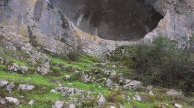 Buracas do Casmilo at Condeixa - Portekiz. Engebeli bir yamaçta yuva yapmış antik kireçtaşı mağaraları, bulutlu bir günde yeşil bitki örtüsü ve yosun kaplı kaya oluşumları arasında birden fazla doğal mağara açıkları barındırır..