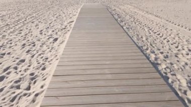 Geniş, ahşap bir patika engin, el değmemiş bir sahil boyunca uzanır, açık mavi gökyüzünün altındaki küçük beyaz bir cankurtaran kulesine uzanır..