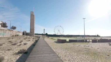 Figueira da Foz, Portekiz - 12 Kasım 2024: Figueira da Foz 'un dönme dolabı, şehrin canlı kıyı sahnesinin bir sembolü, açık mavi gökyüzünün zeminine karşı dik, plajın ve çevrenin panoramik manzarasını sunuyordu..