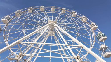 Yükselen beyaz dönme dolap, parlak mavi gökyüzüne karşı dimdik ayakta duruyor, heyecan verici manzaralar ve heyecan verici sürüşler vaat ediyor..