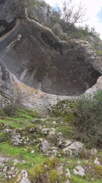 Buracas do Casmilo at Condeixa - Portekiz. Engebeli bir yamaçta yuva yapmış antik kireçtaşı mağaraları, bulutlu bir günde yeşil bitki örtüsü ve yosun kaplı kaya oluşumları arasında birden fazla doğal mağara açıkları barındırır..