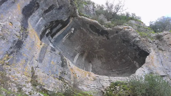 Buracas do Casmilo at Condeixa - Portekiz. Engebeli bir yamaçta yuva yapmış antik kireçtaşı mağaraları, bulutlu bir günde yeşil bitki örtüsü ve yosun kaplı kaya oluşumları arasında birden fazla doğal mağara açıkları barındırır..