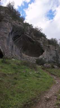 Buracas do Casmilo at Condeixa - Portekiz. Engebeli bir yamaçta yuva yapmış antik kireçtaşı mağaraları, bulutlu bir günde yeşil bitki örtüsü ve yosun kaplı kaya oluşumları arasında birden fazla doğal mağara açıkları barındırır..