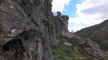 Buracas do Casmilo at Condeixa - Portugal. Ancient limestone caves nestled in a rugged hillside, featuring multiple natural cavern openings amid green vegetation and moss-covered rock formations on a cloudy day. clipart