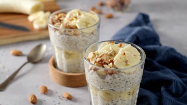 Muz dilimleri ve bademlerle kaplı iki kase yulaf. Bir kaşık, kesme tahtası, bıçak ve yanında mavi bir peçete..