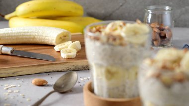 Muz dilimleri ve bademlerle kaplı iki kase yulaf. Bir kaşık, kesme tahtası, bıçak ve yanında mavi bir peçete..