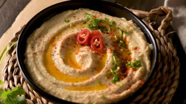 Seramik kasede nefis humus. Siyah ahşap arka planda renkli abur cubur kompozisyonu.