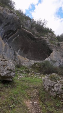 Buracas do Casmilo at Condeixa - Portekiz. Engebeli bir yamaçta yuva yapmış antik kireçtaşı mağaraları, bulutlu bir günde yeşil bitki örtüsü ve yosun kaplı kaya oluşumları arasında birden fazla doğal mağara açıkları barındırır..