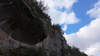 Buracas do Casmilo at Condeixa - Portekiz. Engebeli bir yamaçta yuva yapmış antik kireçtaşı mağaraları, bulutlu bir günde yeşil bitki örtüsü ve yosun kaplı kaya oluşumları arasında birden fazla doğal mağara açıkları barındırır..