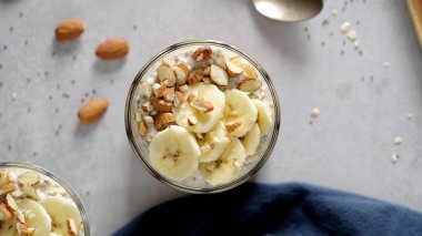 Muz dilimleri ve bademlerle kaplı iki kase yulaf. Bir kaşık, kesme tahtası, bıçak ve yanında mavi bir peçete..